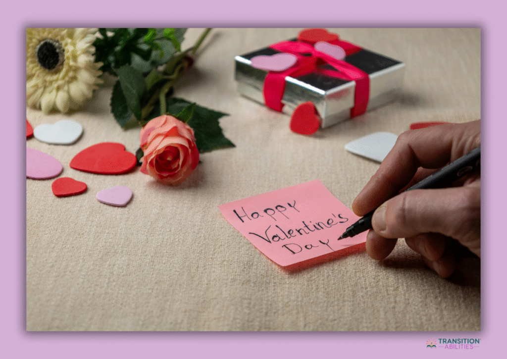 Hand writing a Valentine's Day note beside flowers and gift box