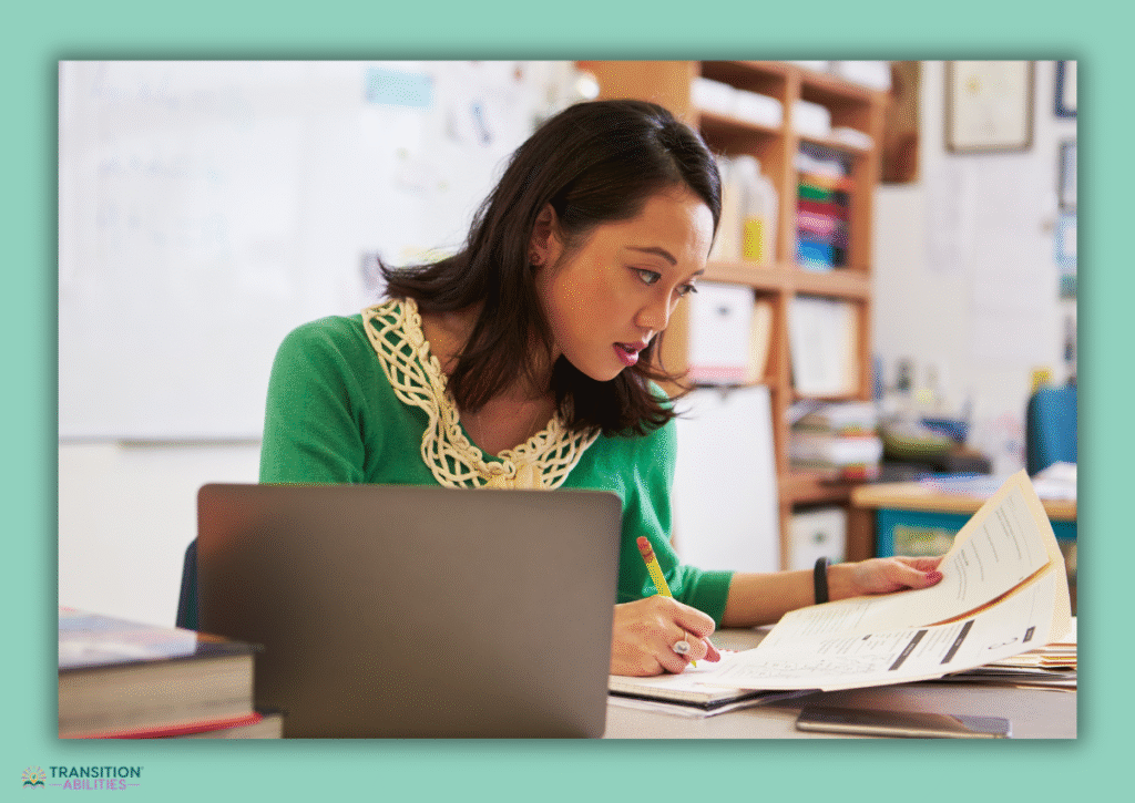 Teacher reviewing paperwork at desk with laptop