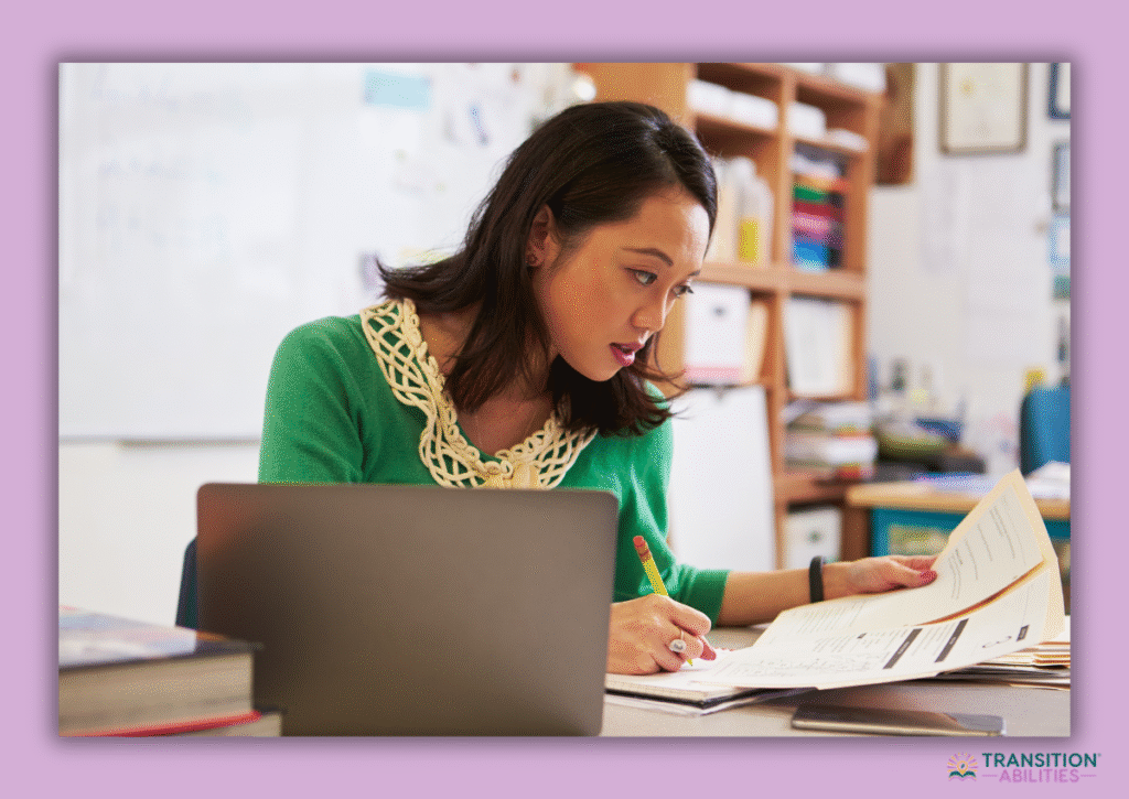 Teacher reviewing paperwork at desk with laptop