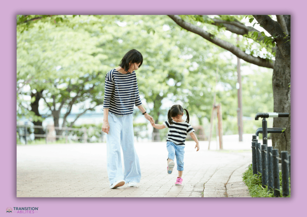 Adult holding a child’s hand while walking outside on a path.