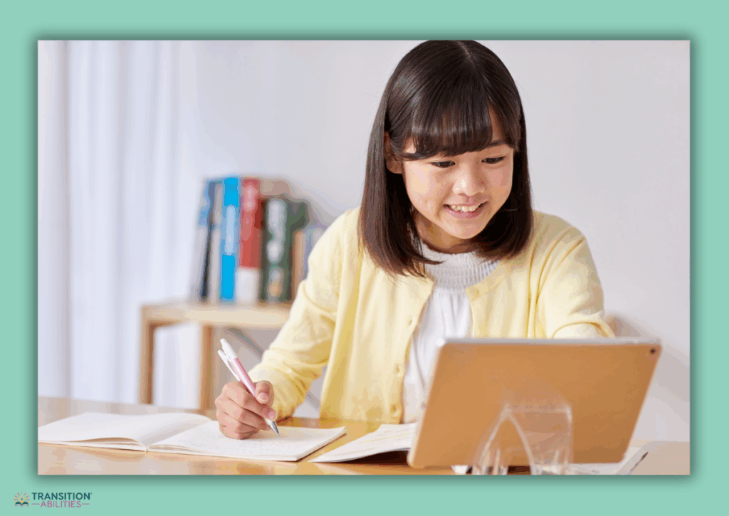 Student writing in a notebook while using a tablet.