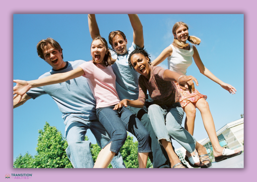 A joyful group of five teenagers posing energetically outdoors under bright sunlight.