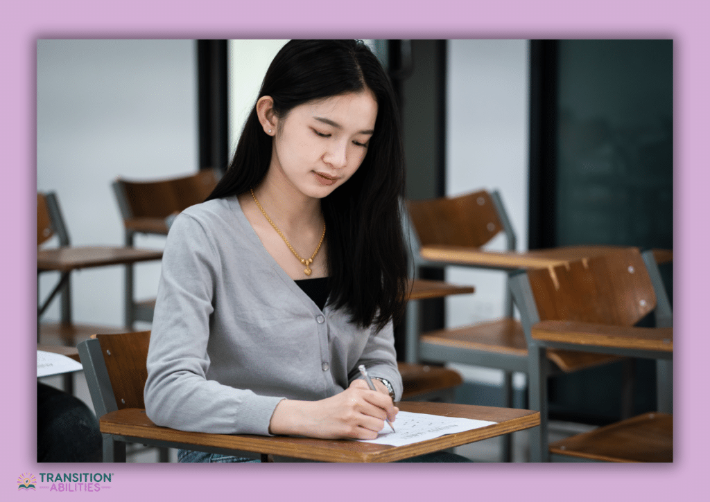 A female student sitting in a classroom, writing on paper during an activity or test.