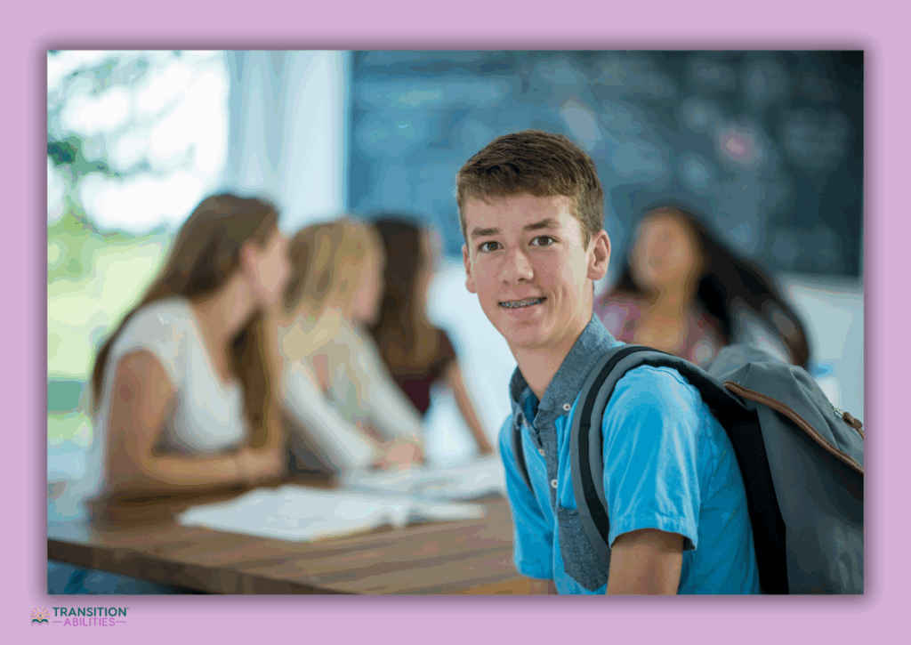 Teen boy smiling at camera while sitting in a classroom with peers in the background